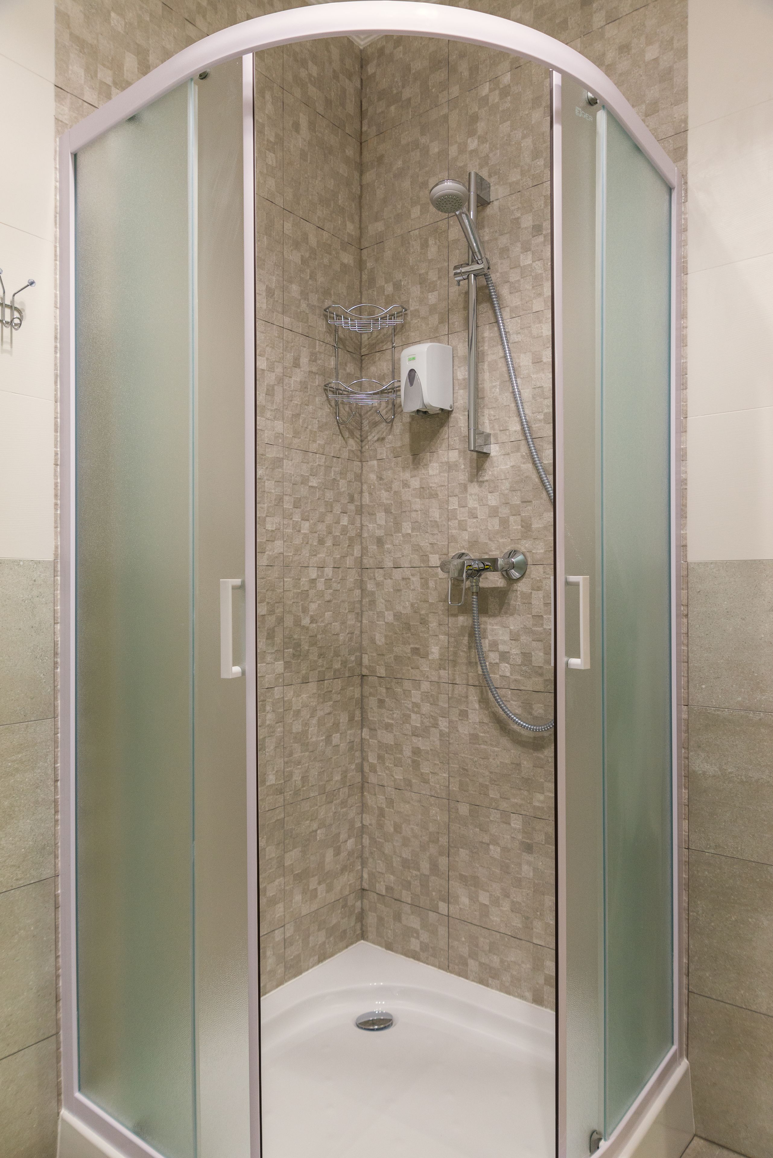 A corner shower with frosted glass doors, a handheld showerhead, a wall-mounted faucet, and a handheld showerhead.