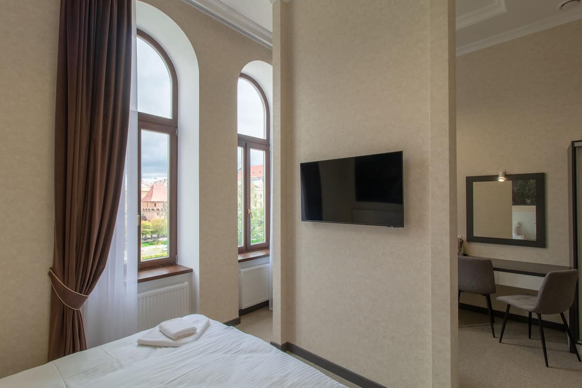 A hotel room with a bed, a desk, a chair, a TV, and large windows with curtains.