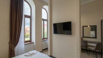 A hotel room with a bed, a desk, a chair, a TV, and large windows with curtains.