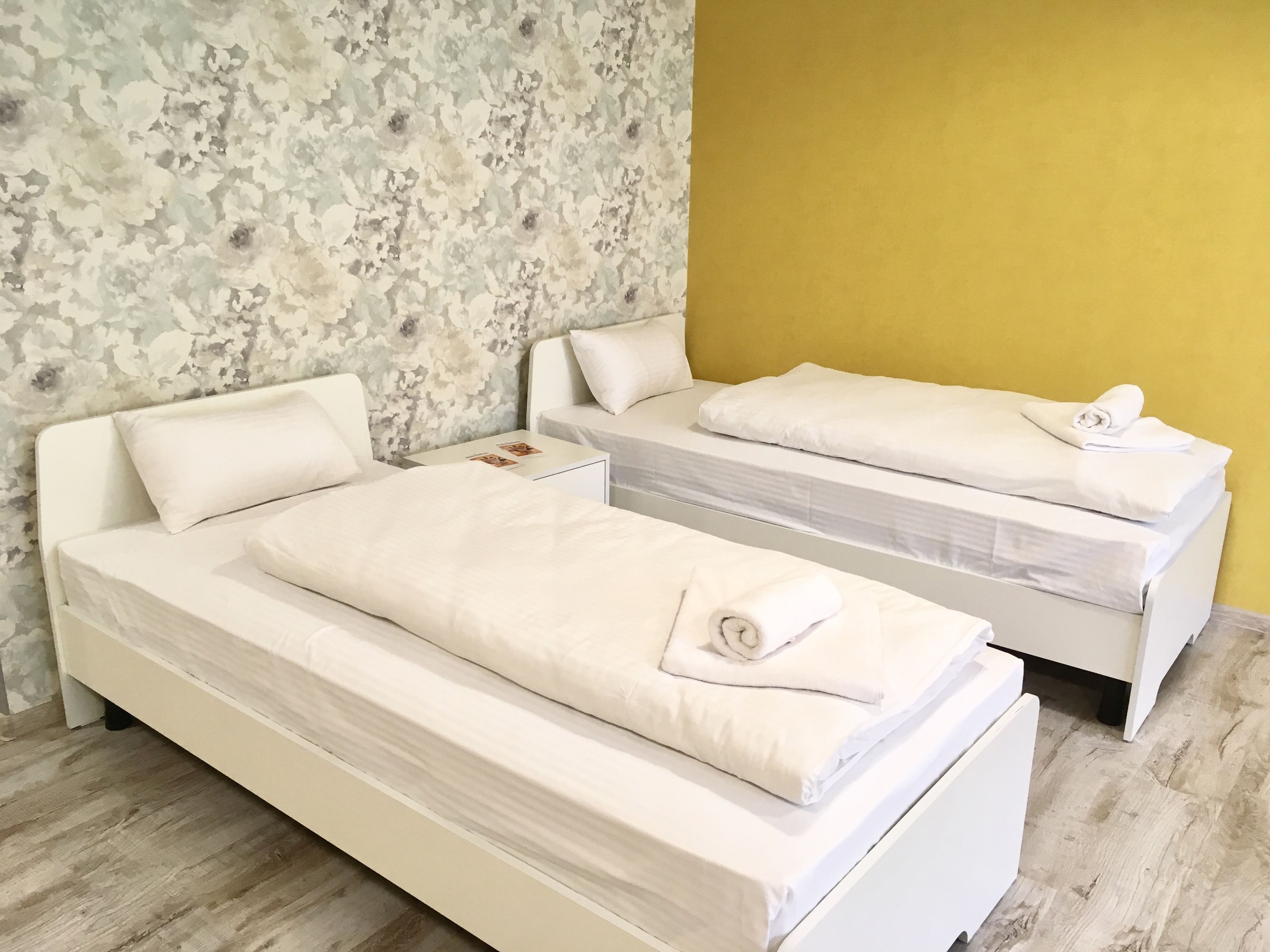 A double bed with white bedding and pillows, a nightstand with a photo, and a yellow wall.