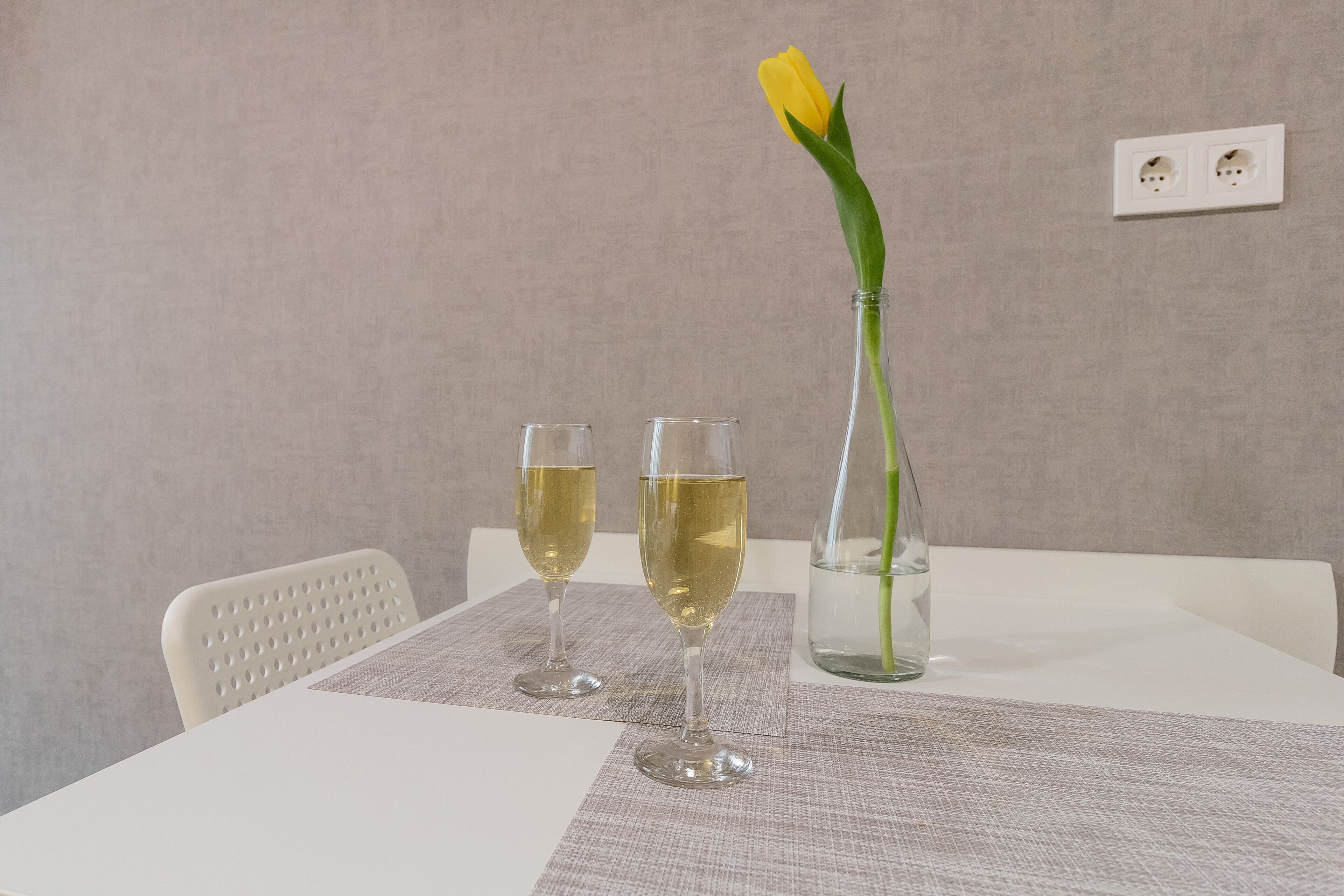 Una mesa con dos copas de vino blanco y un florero con una tulipán amarilla.