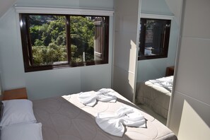 A bedroom with a bed, a window with a view of greenery, and a mirror reflecting the bed.