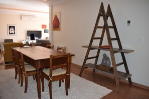 A dining area with a wooden table and chairs, a white rug, and a wooden ladder shelf against the wall.