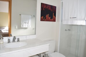 A bathroom with a white sink, two faucets, a mirror, a toilet, and a shower.