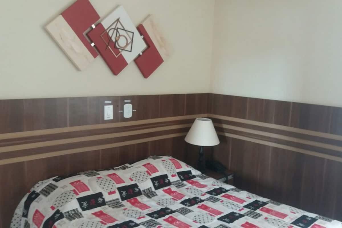 A hotel room with a bed, a nightstand, a lamp, and a wall-mounted artwork.