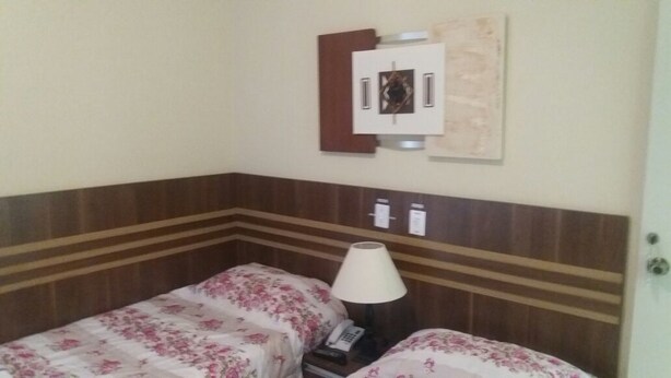 Een hotelkamer met twee bedden, een nachtkastje, een lamp, een telefoon en een lichtschakelaar aan de muur.