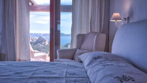 A bedroom with a bed, a chair, a lamp, and a view of a lake and mountains. - Luxury Villa's Valle dell'Erica (Santa Teresa di Gallura)