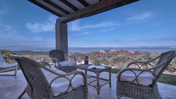A covered outdoor seating area with wicker furniture and a view of the sea and distant landscape. - Luxury Villa's Valle dell'Erica (Santa Teresa di Gallura)