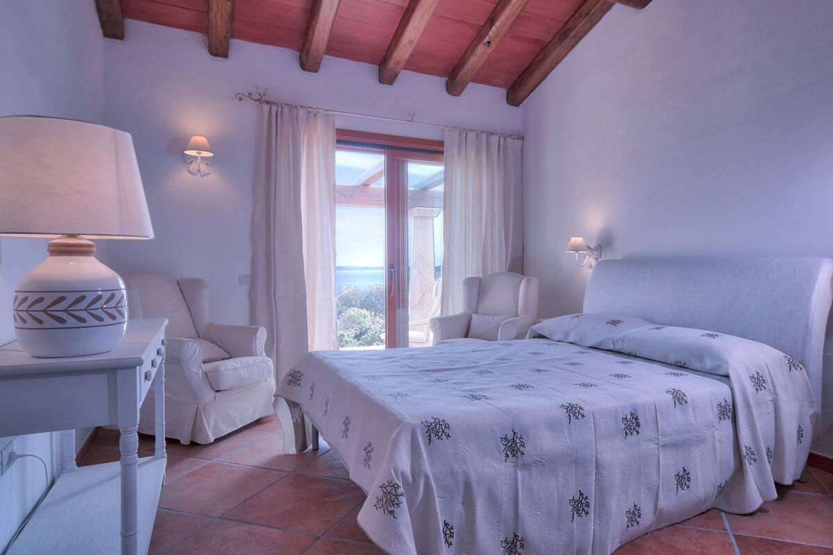 Ein Schlafzimmer mit einem Bett, zwei Stühlen, einem Nachttisch und einer Lampe.