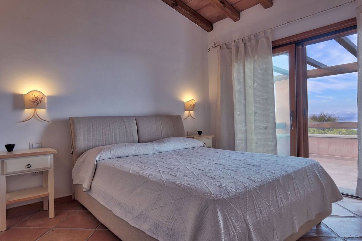 Ein Schlafzimmer mit Bett, Nachttischen und Blick durch eine Glastür.