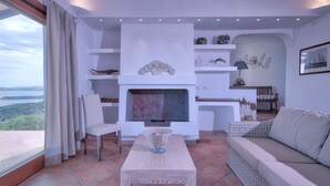 A modern living room with a fireplace, white furniture, and decorative items. - Luxury Villa's Valle dell'Erica (Santa Teresa di Gallura)