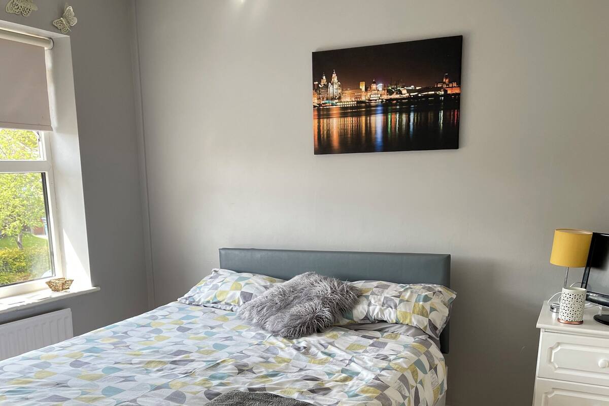 A bedroom with a bed, a nightstand, a lamp, and a window with a view of a cityscape.