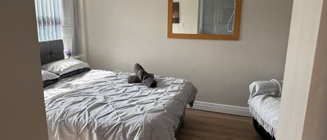 A bedroom with a bed, a nightstand, a mirror, and a window with curtains.