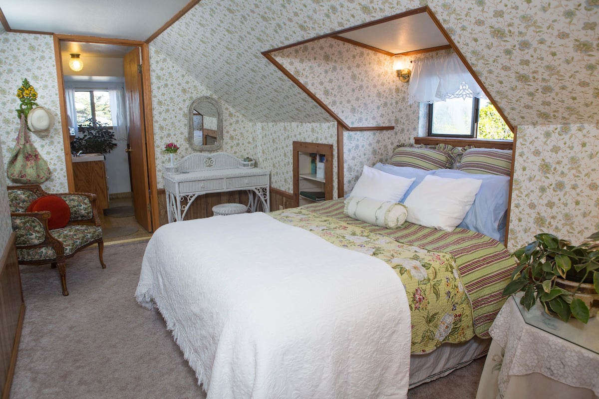 A bedroom with a four-poster bed, a desk, a chair, and a window with a view.