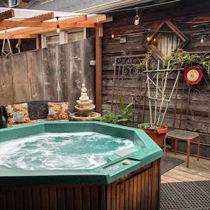 A hot tub in a rustic outdoor setting with wooden walls, a wooden pergola, and a decorative metal fence. - Country Inn Bed and Breakfast (Fort Bragg)