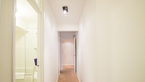 Un couloir étroit, avec une cabine de douche en verre sur le côté gauche, une porte au fond et un sol recouvert de moquette.