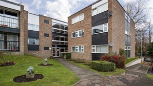 Un immeuble d’appartements moderne avec une façade en briques, de grandes fenêtres et une pelouse bien entretenue agrémentée de parterres de fleurs.