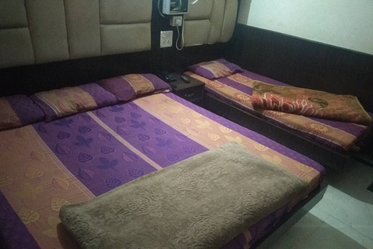 A hotel room with two beds, each with purple and orange bedding. There is a telephone on the wall and a small table with a remote control.