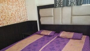 A bed with a patterned bedspread and two pillows, a headboard, and a patterned wall. - Hotel Silver Palace - Hostel (New Delhi)