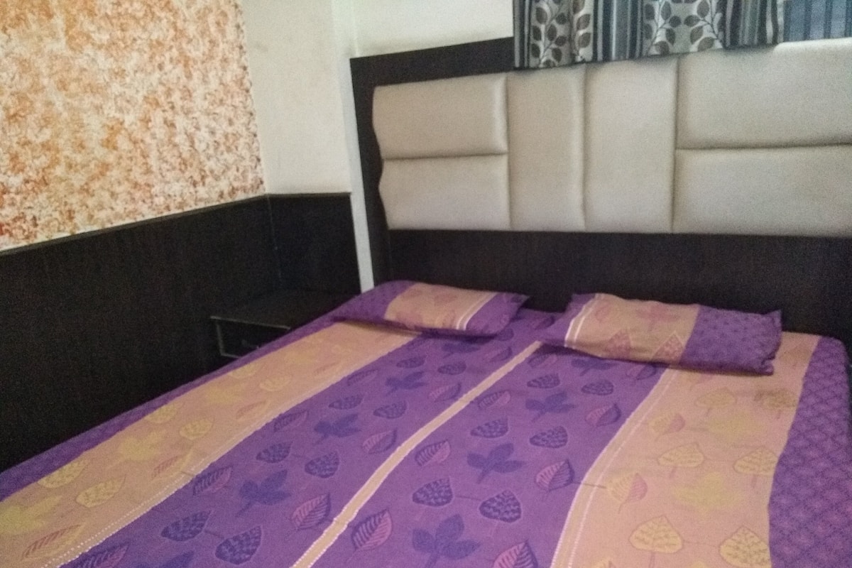 A bed with a patterned bedspread and two pillows, a headboard, and a patterned wall.