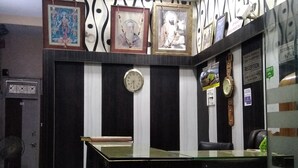A reception area with a reception desk, a clock, framed pictures on the wall, and a fan. - Hotel Silver Palace - Hostel (New Delhi)