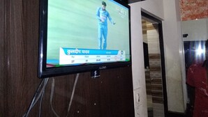 A television mounted on a wall displaying a cricket match. - Hotel Silver Palace - Hostel (New Delhi)