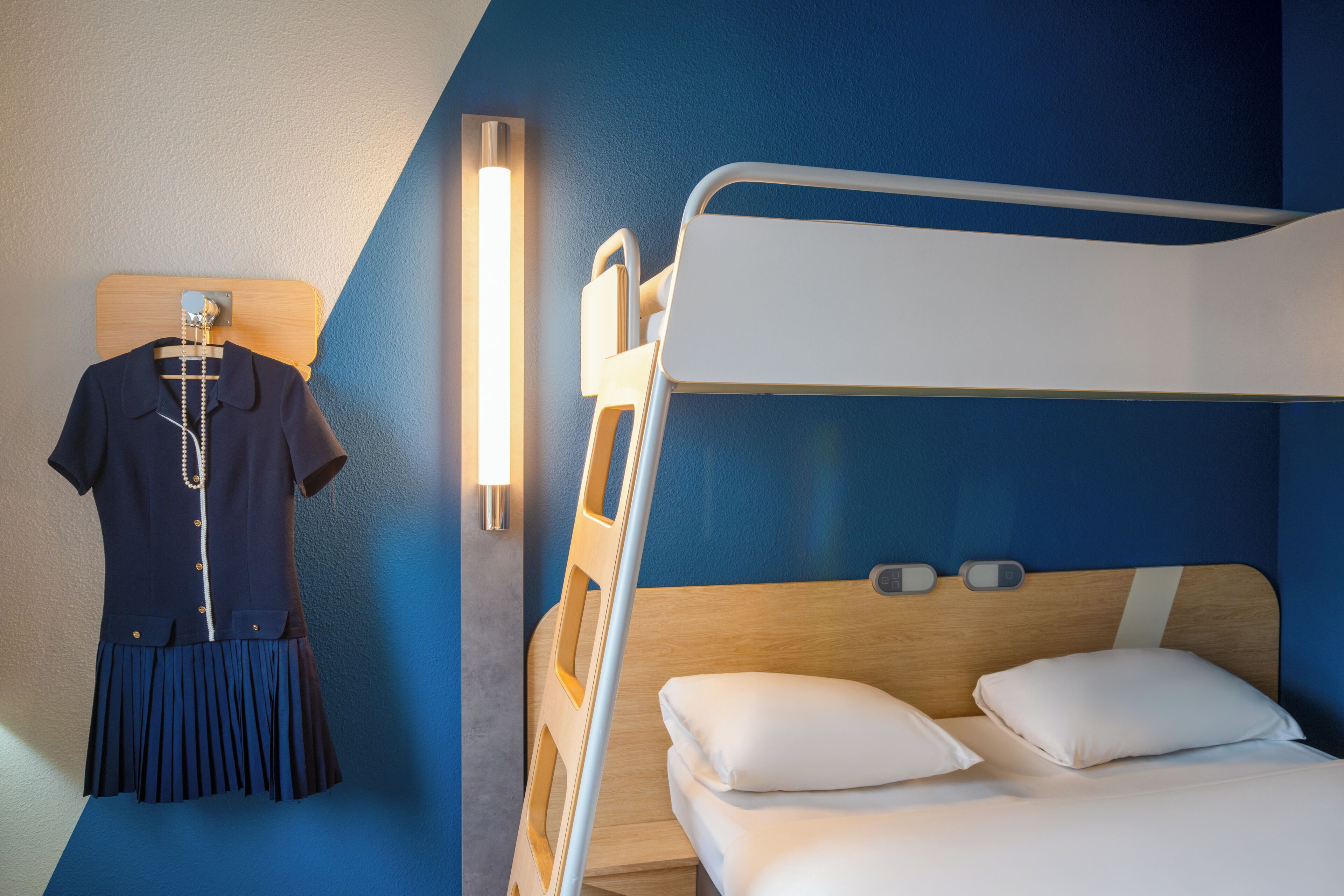 Une chambre d’hôtel avec un lit superposé, un portant à vêtements et un luminaire fixé au mur.