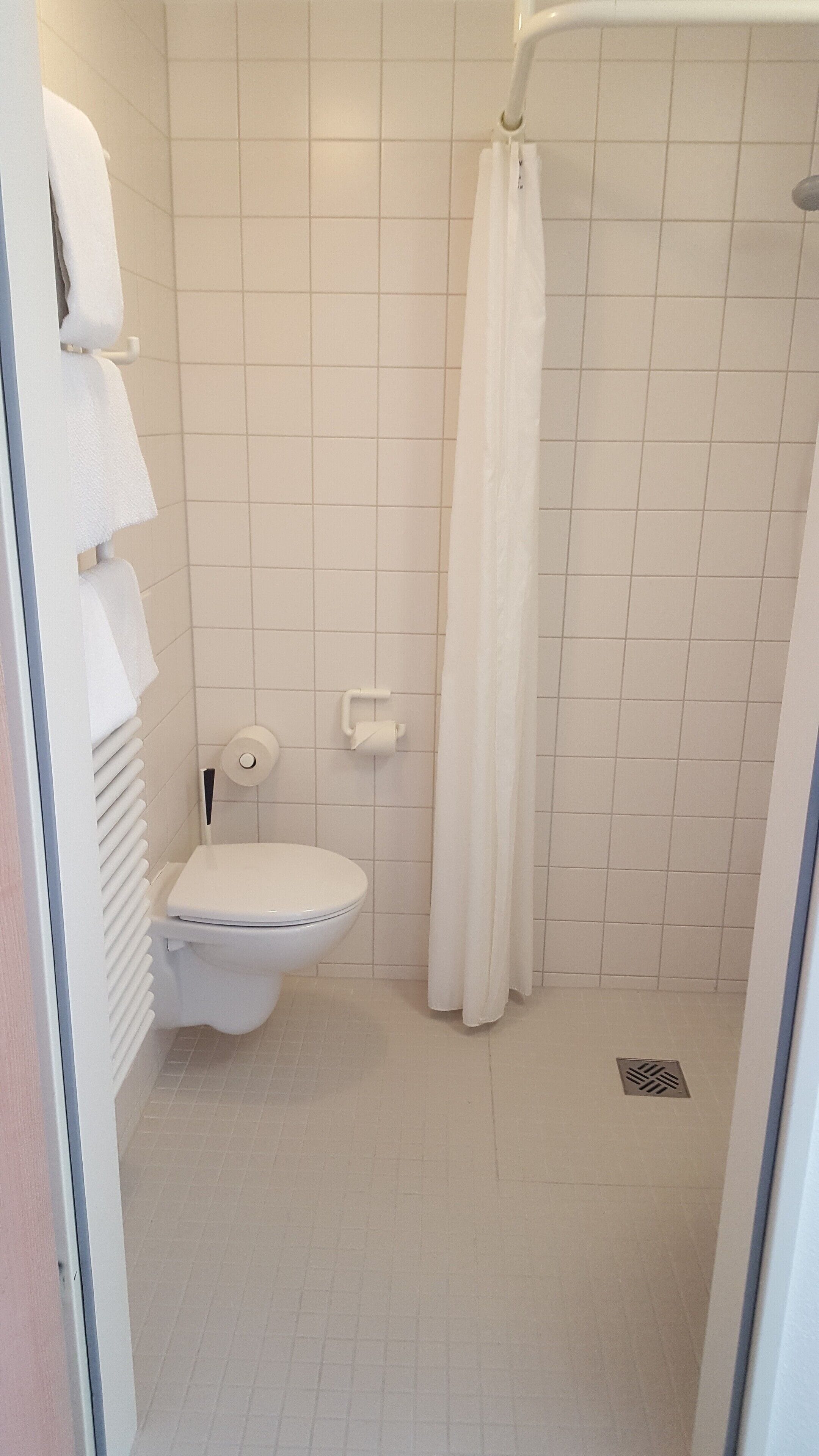 A small, white bathroom with a toilet, a shower curtain, and a towel rack.