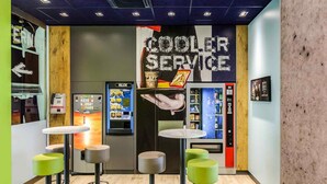 A modern bar area with stools, a 'COOLER SERVICE' sign, and vending machines. - Ibis Budget Salzburg Airport (Wals-Siezenheim)