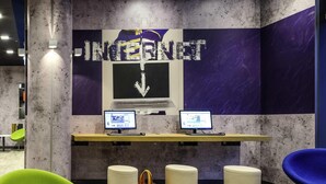 A modern workspace with two computers, a purple and white wall with 'INTERNET' text, and a green chair. - Ibis Budget Salzburg Airport (Wals-Siezenheim)