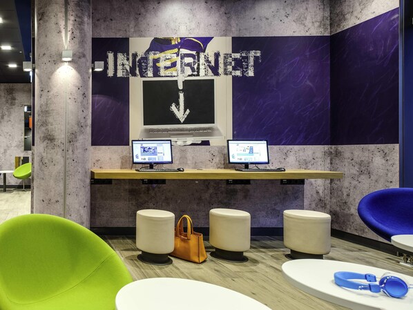 Ein moderner Arbeitsplatz mit zwei Computern, einer violett-weißen Wand mit dem Schriftzug 'INTERNET' und einem grünen Stuhl.