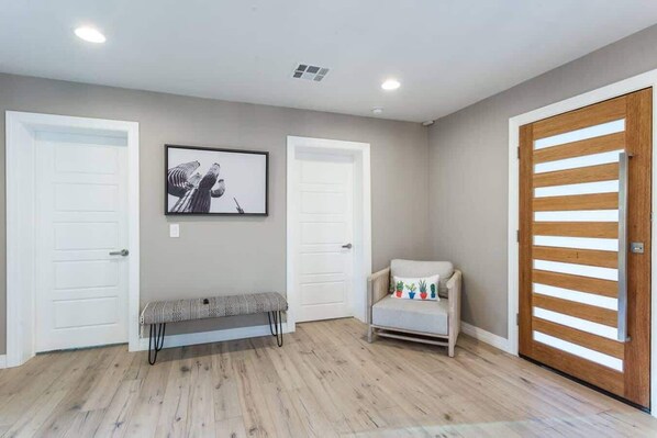 Une pièce avec deux portes blanches, un banc, une chaise avec un coussin et un tableau encadré au mur.
