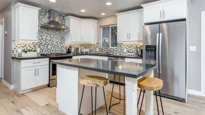 A modern kitchen with white cabinets, a stainless steel refrigerator, and a black countertop island with stools. - Modern Living, A Fav! Firepit, BBQ, Min to Airport (Phoenix)