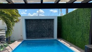 A swimming pool with a waterfall feature, surrounded by a wooden deck and lounge chairs. - Hotel Apartamentos Stone (Bacalar)