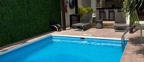 Une piscine agrémentée d’une pergola, de chaises longues et d’un espace bar.