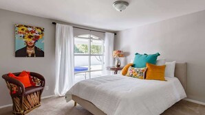 Een slaapkamer met een groot bed, een stoel, een raam met gordijnen en een schilderij aan de muur.