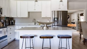 Een moderne keuken met witte kastjes, roestvrijstalen apparatuur en een centraal eiland met krukken.