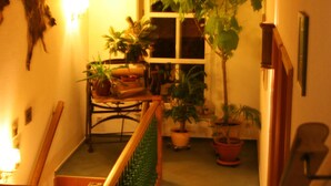 A hallway with a wooden staircase, potted plants, and a window. - Hammers Landhotel Gmbh (Teltow)