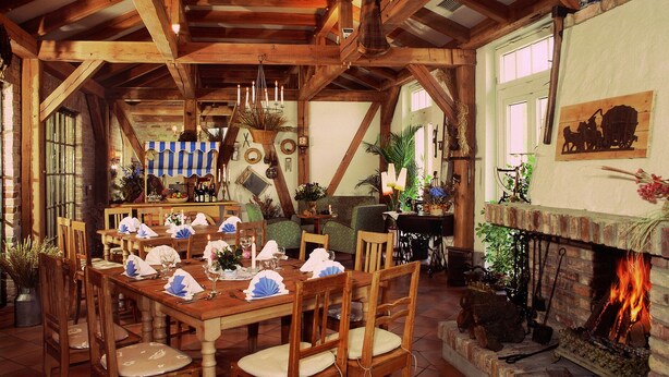 A rustic dining room with wooden beams, a fireplace, and a dining table set for a meal. - Hammers Landhotel Gmbh (Teltow)