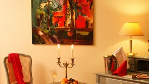 A room with a chair, a table with fruit and a glass, a lamp, and a painting on the wall. - Hammers Landhotel Gmbh (Teltow)