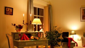 A hotel room with a bed, a desk with a lamp, a chair, a potted plant, and a window with curtains. - Hammers Landhotel Gmbh (Teltow)