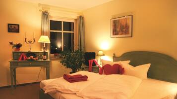 Una habitación de hotel con cama, escritorio con lámpara, planta y ventana con cortinas.