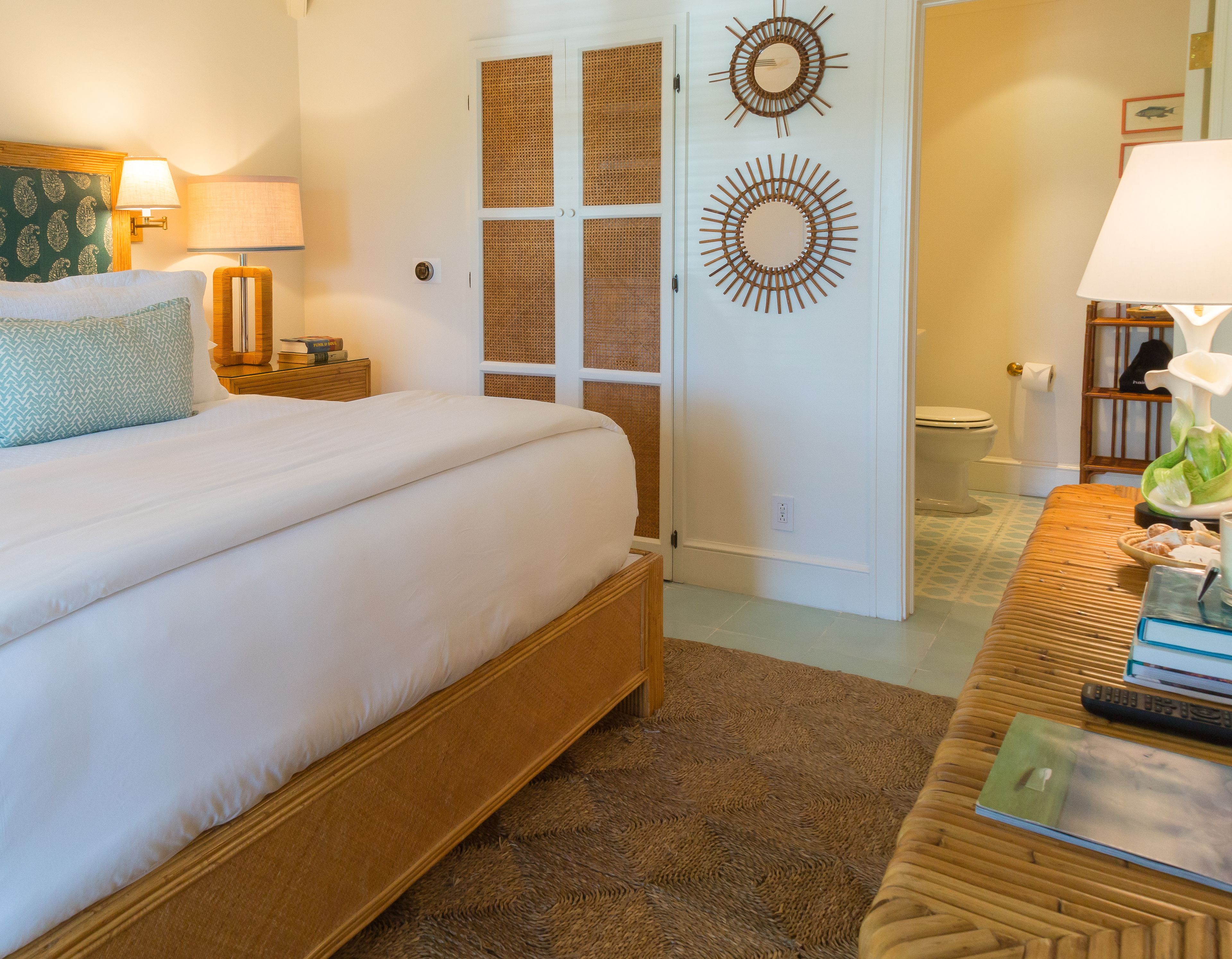 A neatly arranged bedroom with a large bed, a bedside table with a lamp, a wooden bench, and two decorative wall mirrors.
