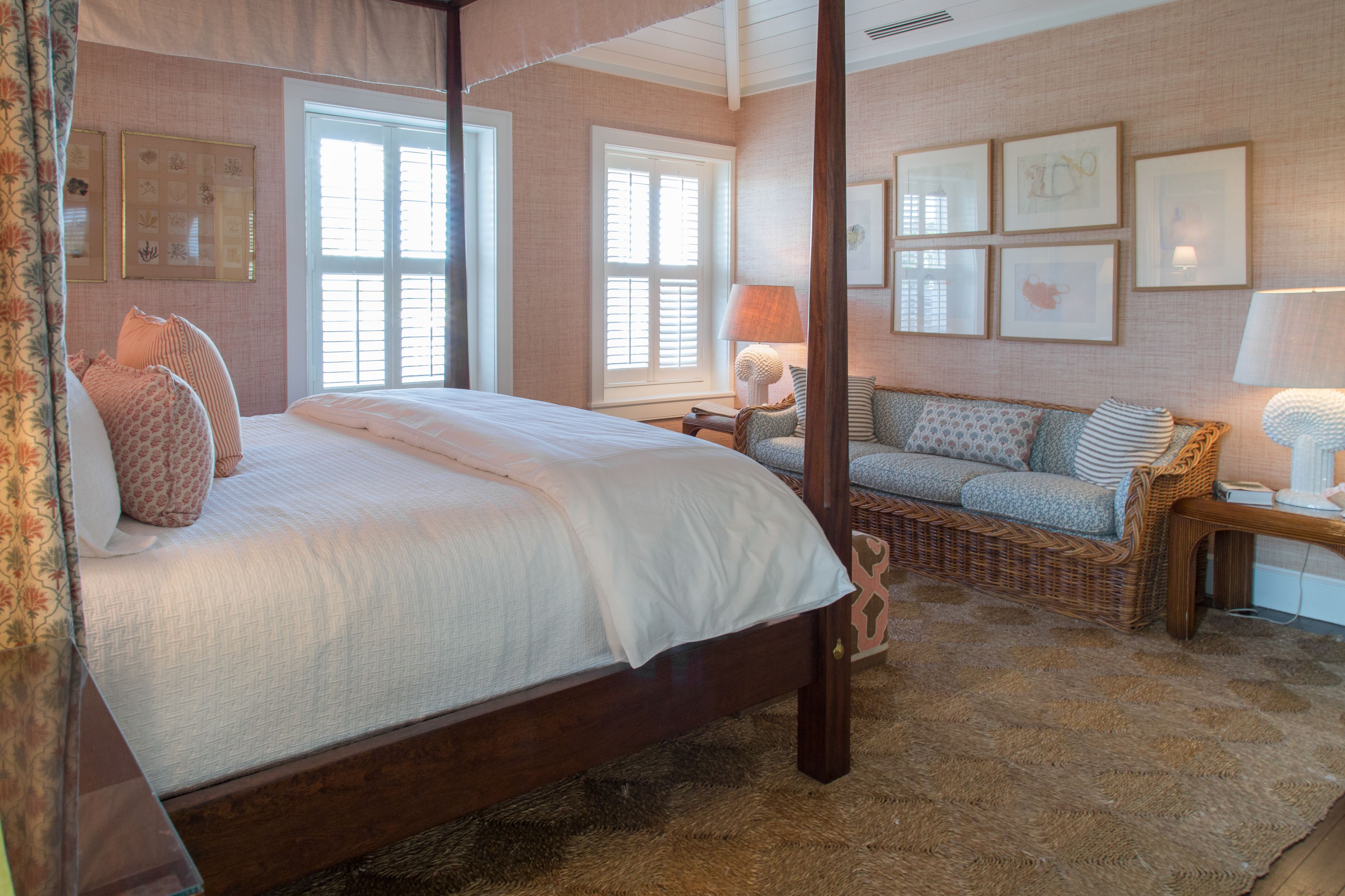 A four-poster bed with a wooden frame, a sofa with patterned cushions, and a wicker side table with a lamp.