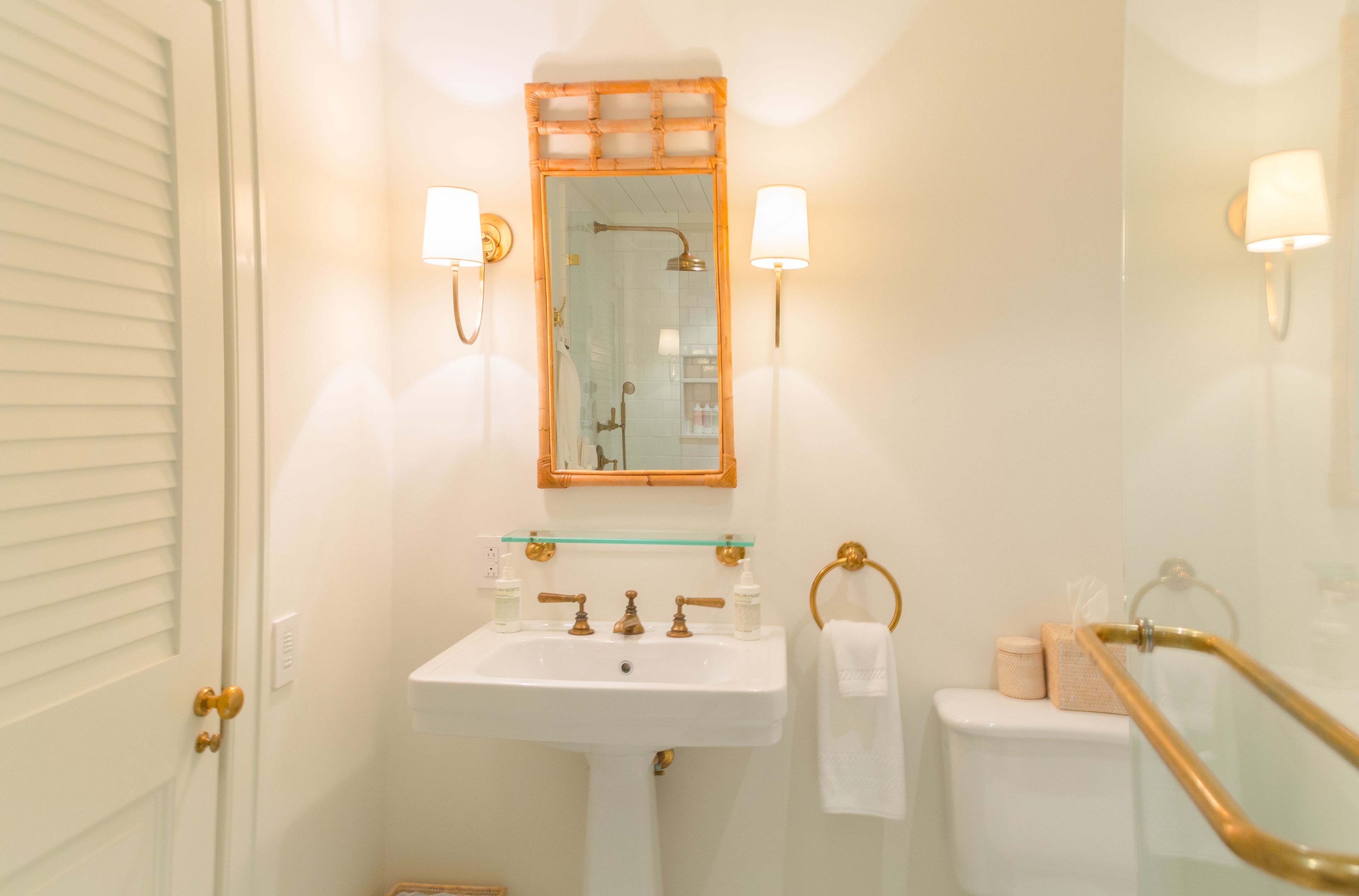 A bathroom with a white sink, a glass shelf above it, a mirror with a wooden frame, and two wall-mounted lights.