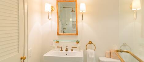 A bathroom with a white sink, a glass shelf above it, a mirror with a wooden frame, and two wall-mounted lights.