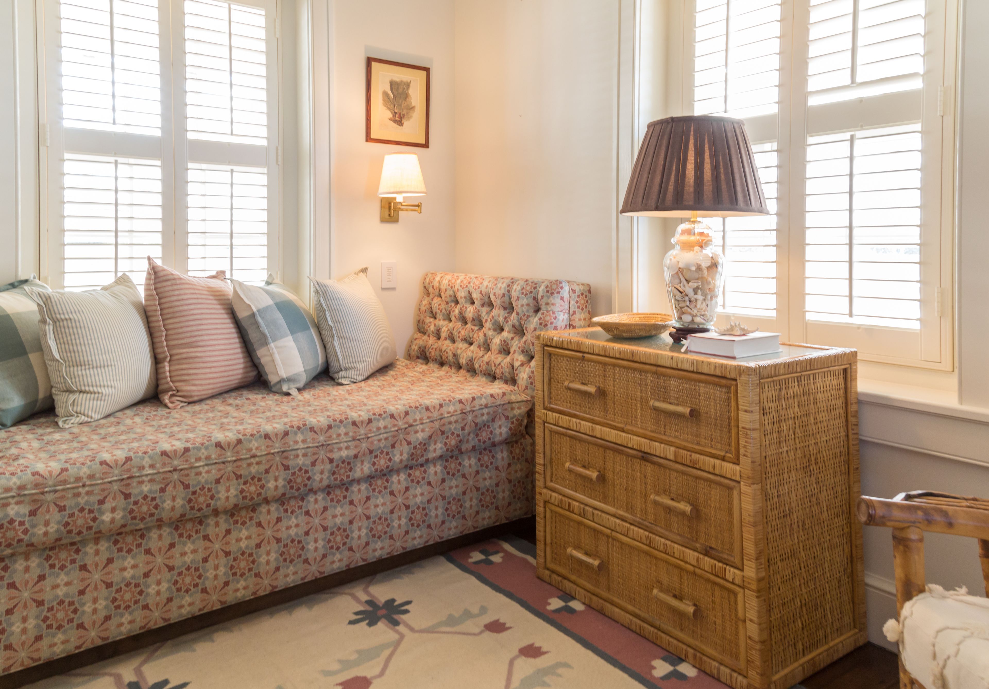 A cozy room with a patterned sofa, a wicker chest of drawers, and a lamp on a side table.