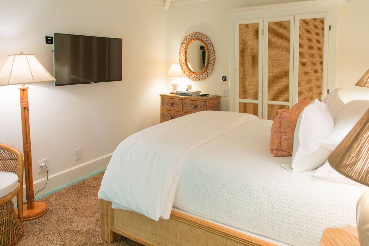 Un dormitorio con cama, televisor montado en la pared, cómoda, espejo y lámpara.