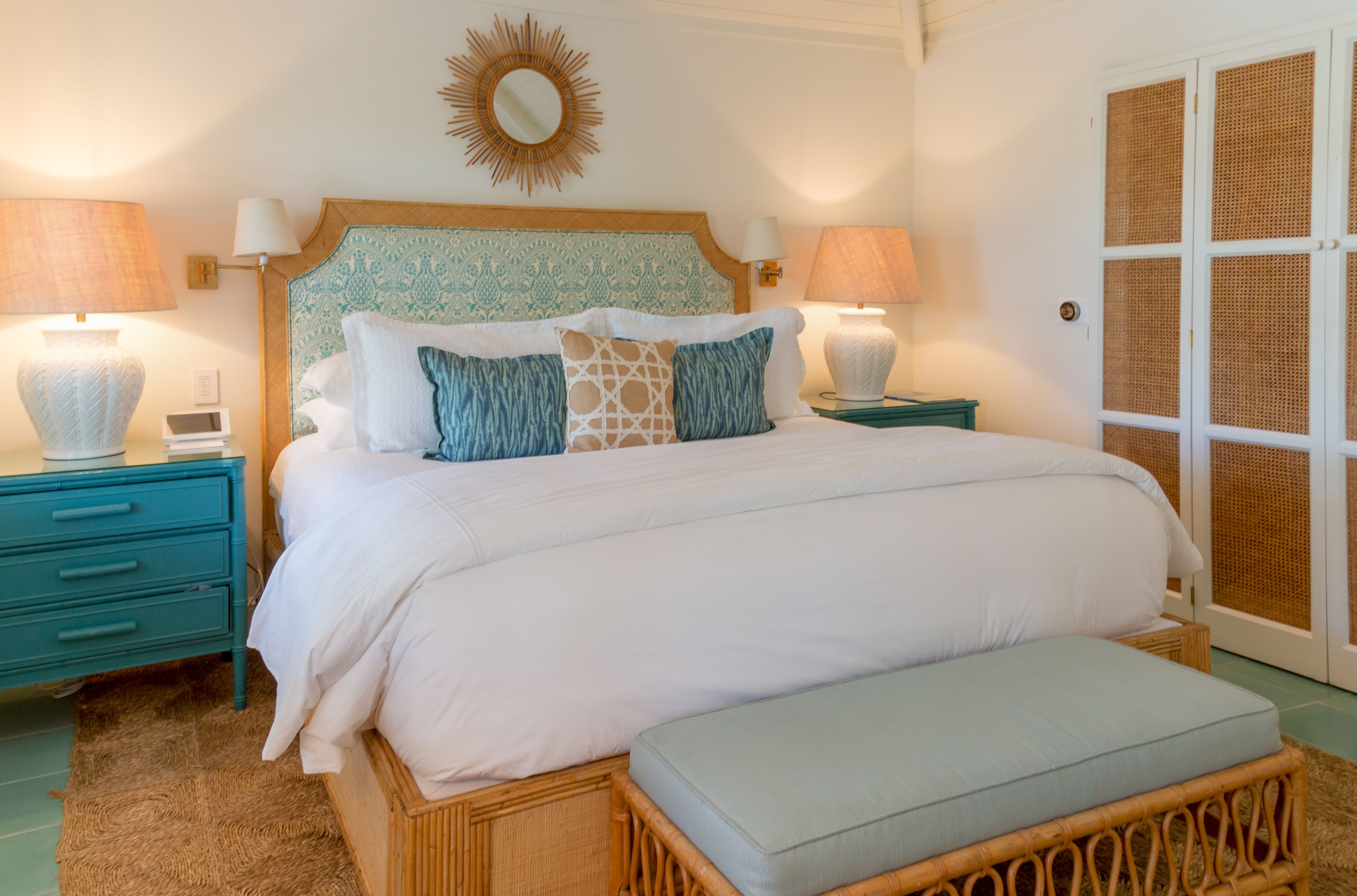 Een netjes opgemaakt slaapkamer met een bed, nachtkastjes, een bankje en een decoratieve spiegel.