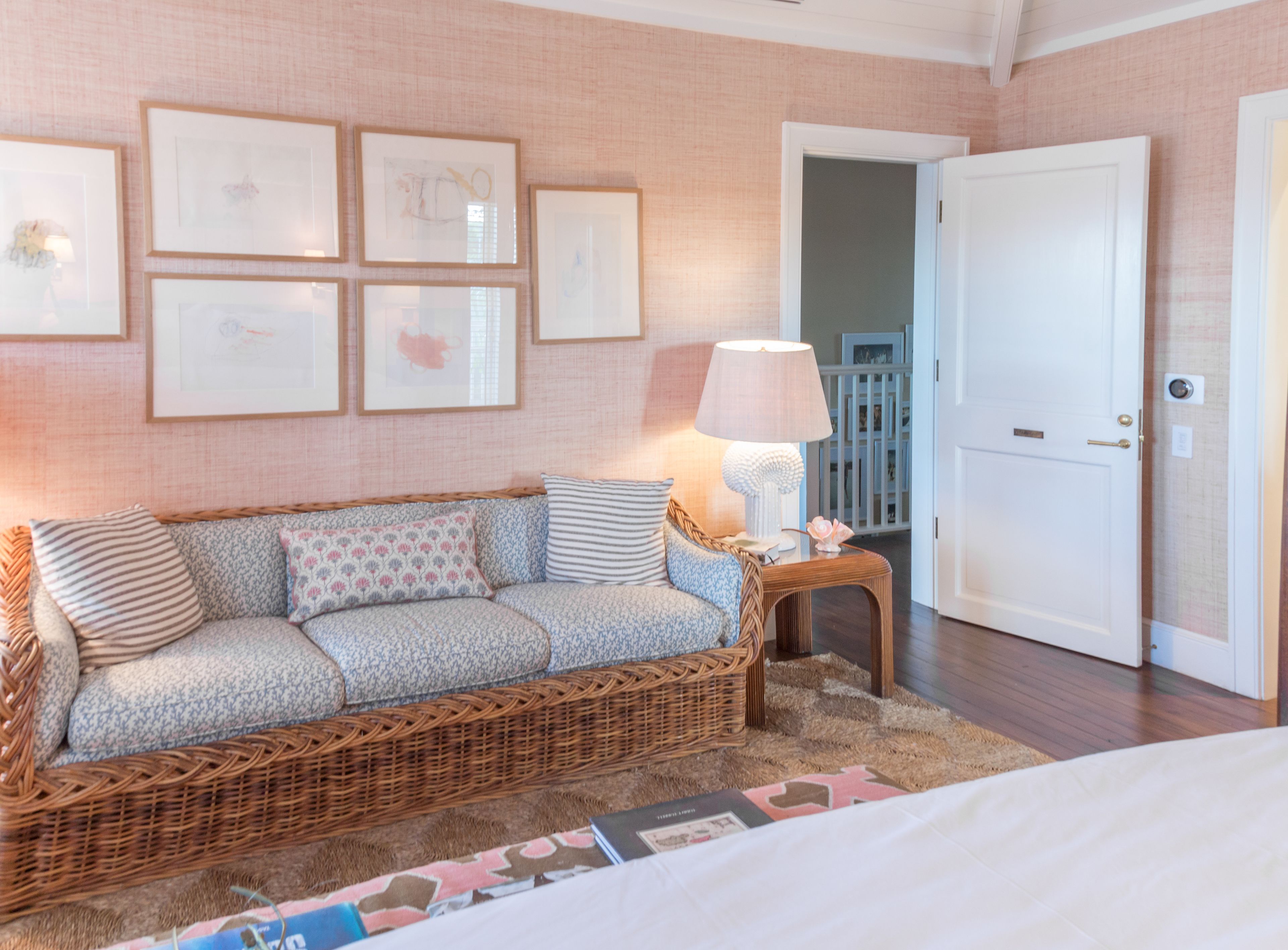 A cozy room with a wicker sofa, a small side table with a lamp, and framed artwork on the wall.